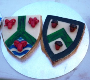 Sotelties of macaroon cooked in the shape of a shield, and marzipan, rolled flat and painted, with elements of Baron Osgot of Corfe and Baroness Esla of Ifeld 's heraldry done in three dimensions. Made by Baroness Blodeuwedd y Gath. Photo by Lady Ursula Von Memmingen, April 2014